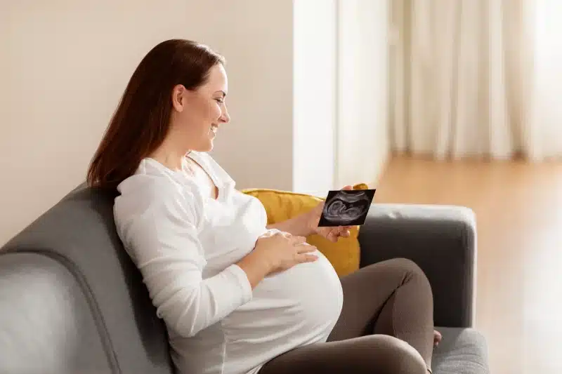 Pregnant woman smiling on a couch while holding an ultrasound photo at ProHealth Chiropractic Rockville clinic