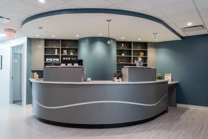 Curved reception desk with wood shelving and pendant lighting at ProHealth Chiropractic Rockville clinic