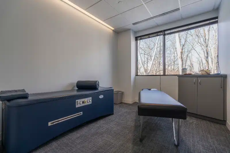 Empty treatment room with adjustment tables and a large window overlooking trees at ProHealth Chiropractic Rockville clinic
